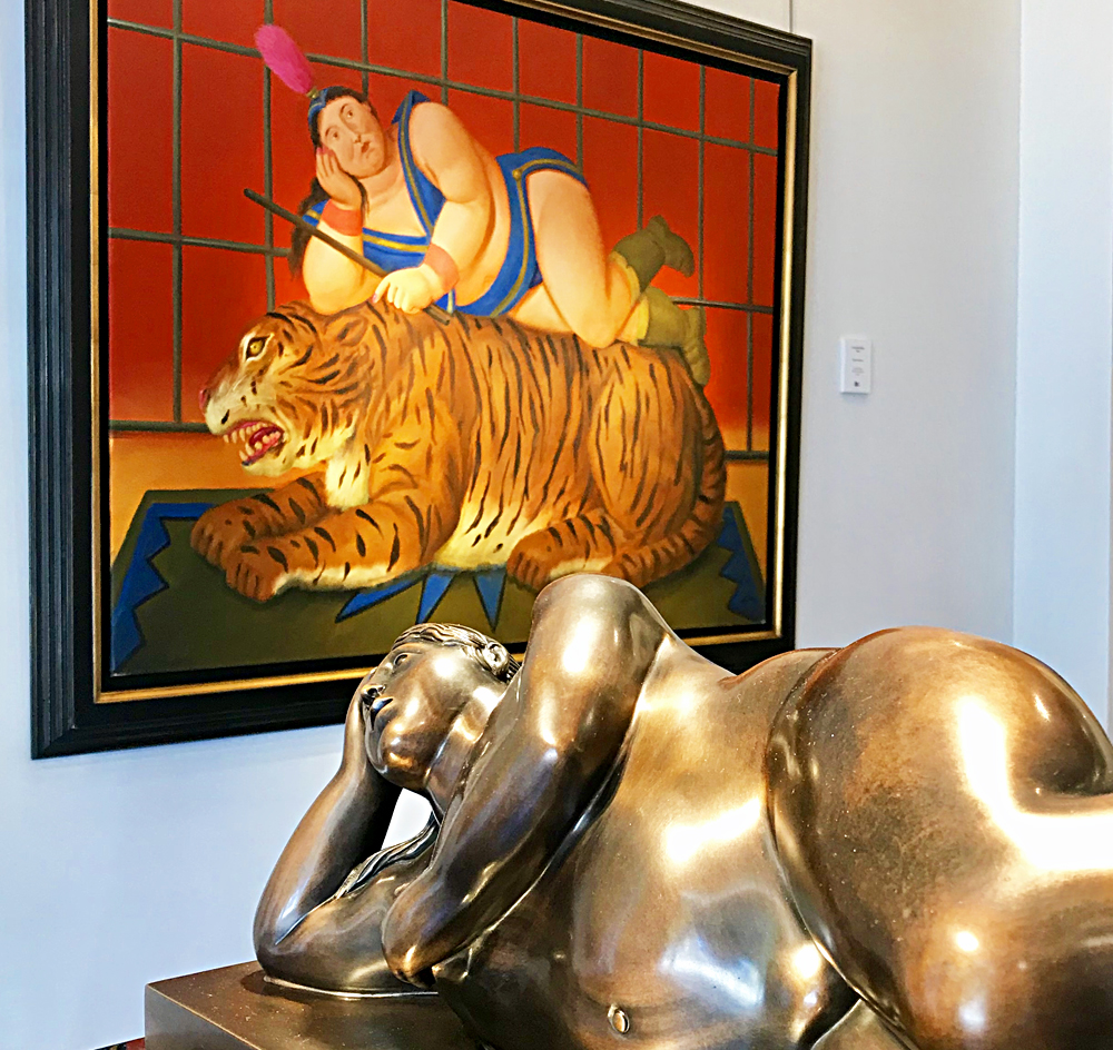 Fernando Botero: Reclining Nude, bronze 1996 et en arrière plan Trainer with Tiger, huile sur toile 2007, exposé à la Galerie Bartoux de Monaco. Photo (c) Charlotte Longépé.