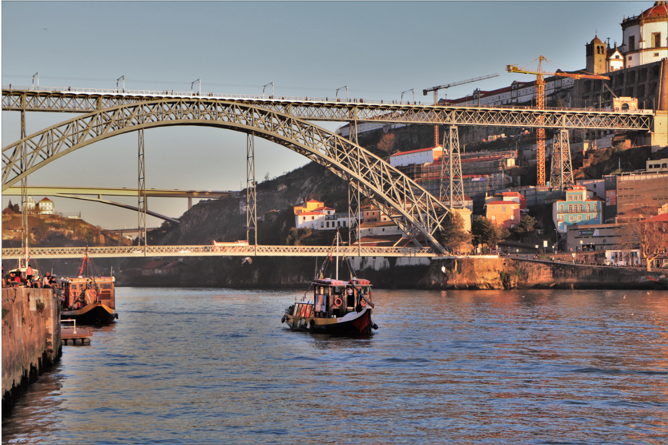 Un bateau traditionnel navigue sur le Douro, à Porto. Il s'apprête à passer sous le plus célèbre pont de la ville, le Ponte Luis 1, dominé par le Claustros do Mosteiro da Serra do Pilar (en haut à droite). / © E.V.